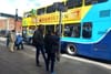 A Dublin Bus stop on Thomas Street, and some people stand in clusters by a pole waiting for it.